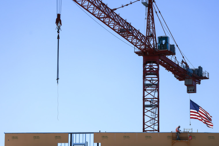 An American flag flies from a crane near a construction worker during construction of a new building.